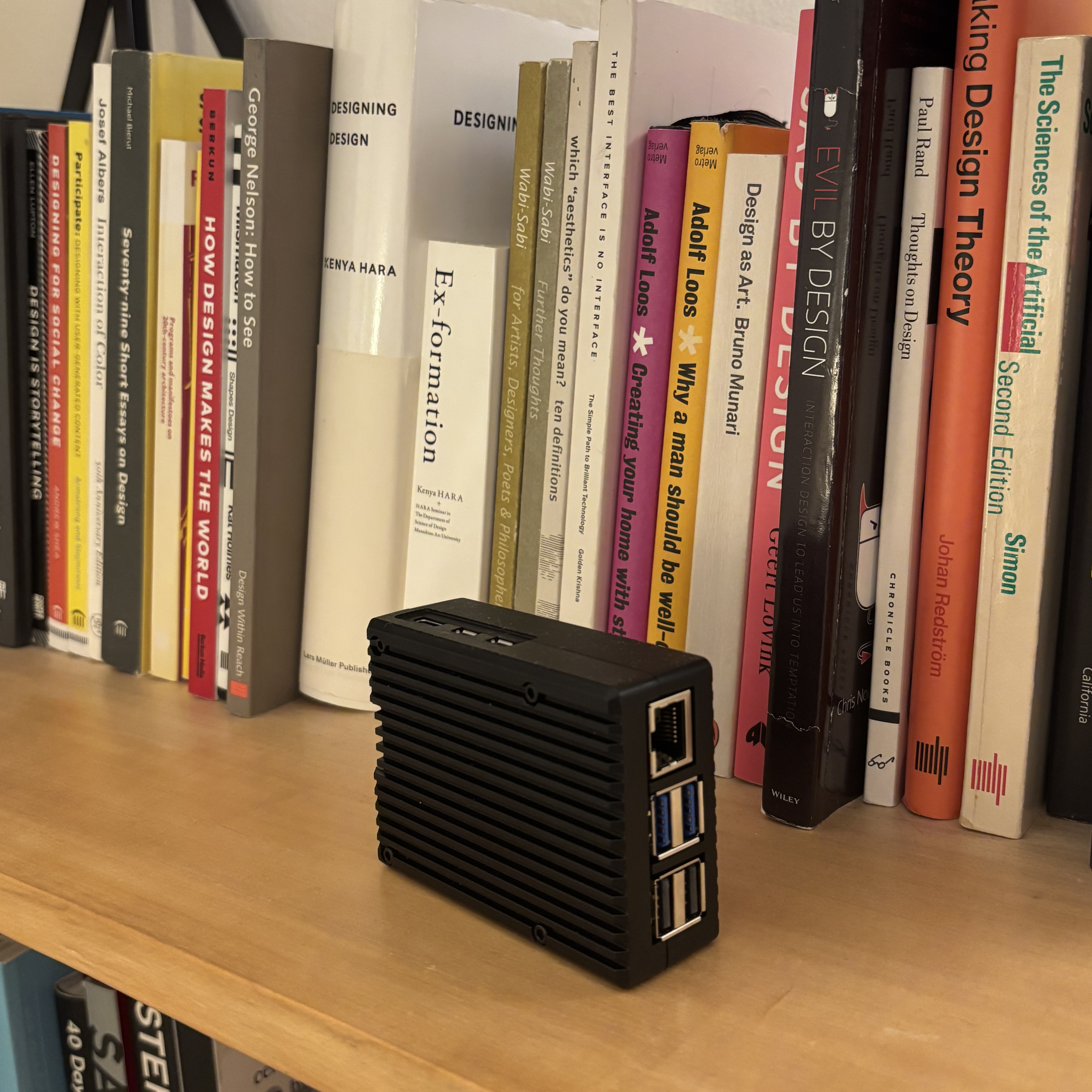 Raspberry Pi 5 in a black aluminium case, sitting on a shelf in front of a design book collection